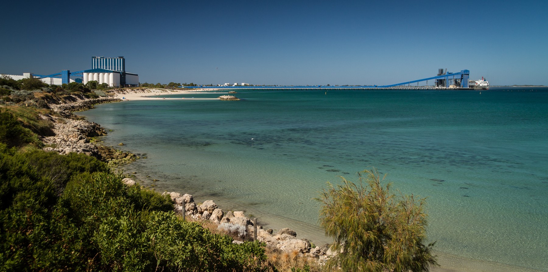 Grain silos on the coast and a long loading structure extending over the water.