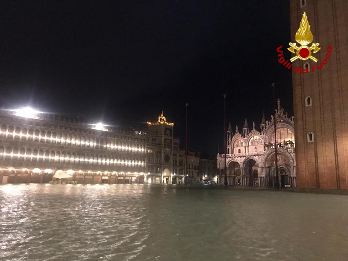 Water covers St Mark’s Square at night beneath the illuminated basilica and campanile